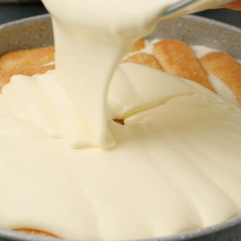 Mascarpone filling being poured over soaked ladyfingers to make tiramisu cake.