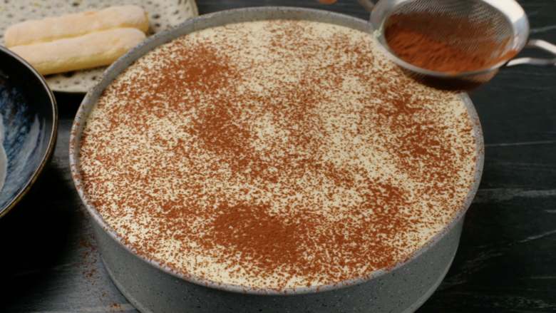 Cocoa powder being dusted on top of tiramisu cake.