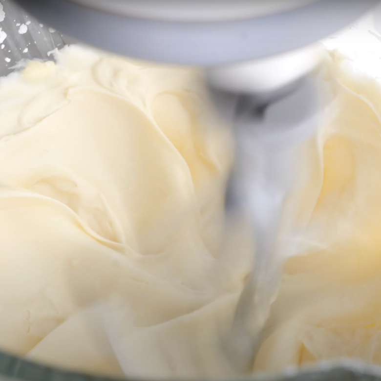 Cinnamon roll icing being mixed together in the bowl of a stand mixer.