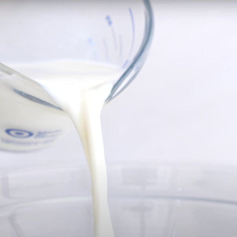 Milk being poured into a mixing bowl to make cinnamon roll dough.