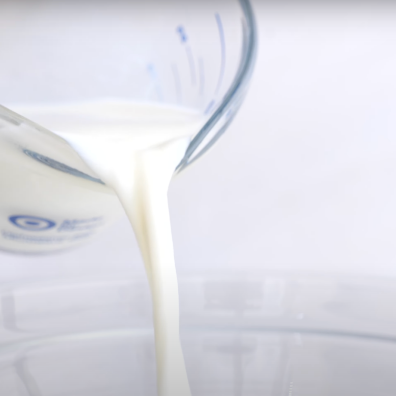 Milk being poured into a mixing bowl to make cinnamon roll dough.