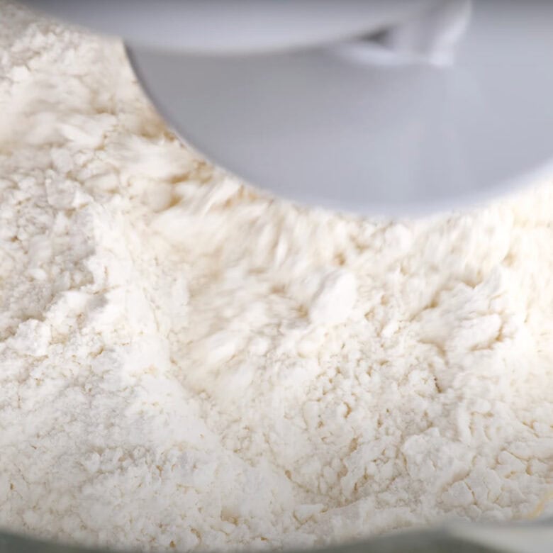 Flour mixture being mixed in a bowl of a stand mixer to make cinnamon roll dough.