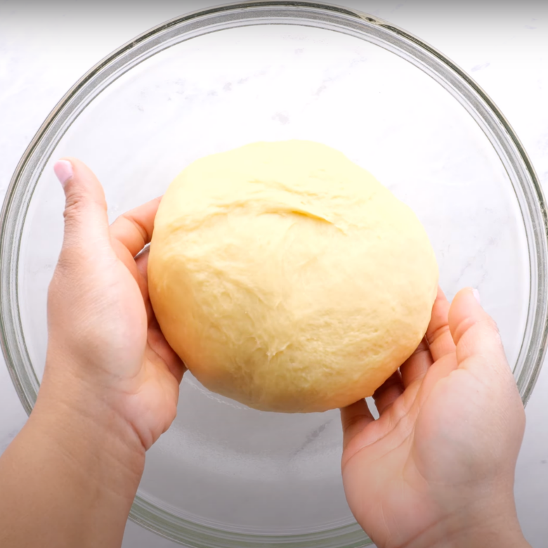 A ball of cinnamon roll dough being placed in a lightly oiled bowl.