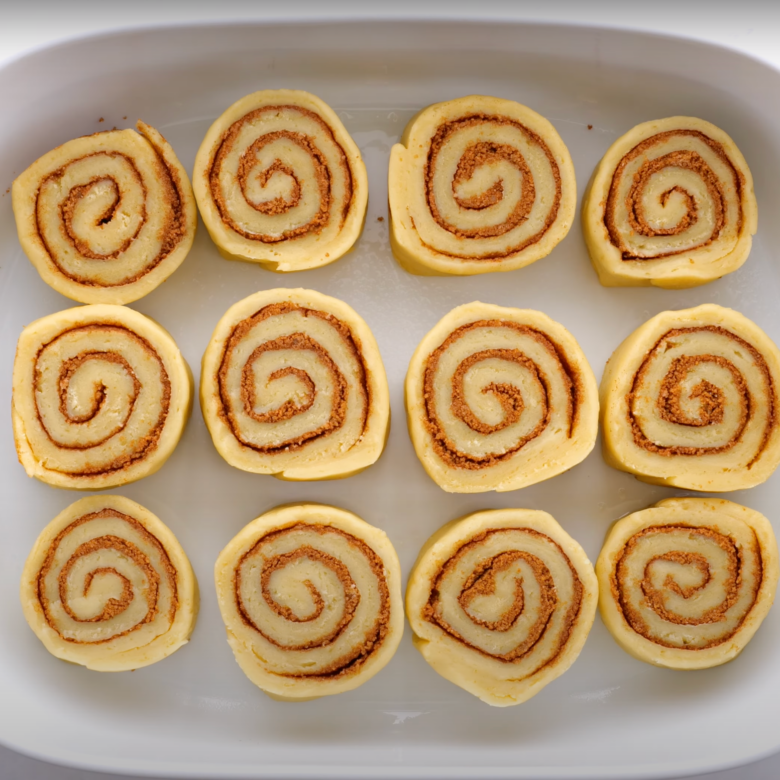 A dozen unbaked cinnamon rolls in a greased baking dish.