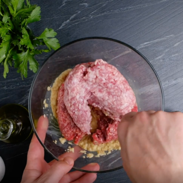 Overhead shot of ground pork and beef being mixed into bread and egg mixture to make Swedish meatball mixture.