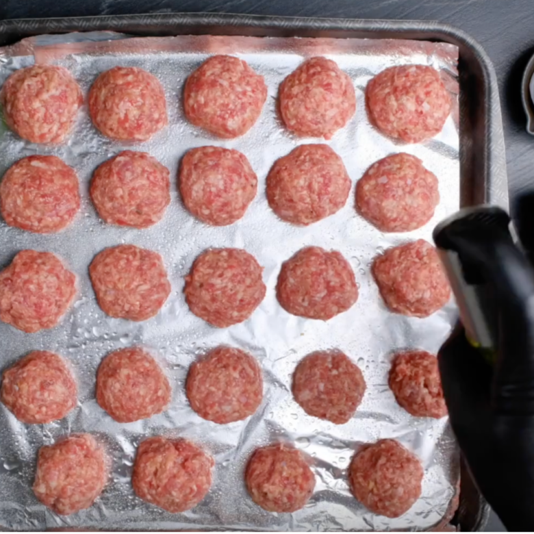 A large rimmed sheet pan lined with foil with uncooked Swedish meatballs.