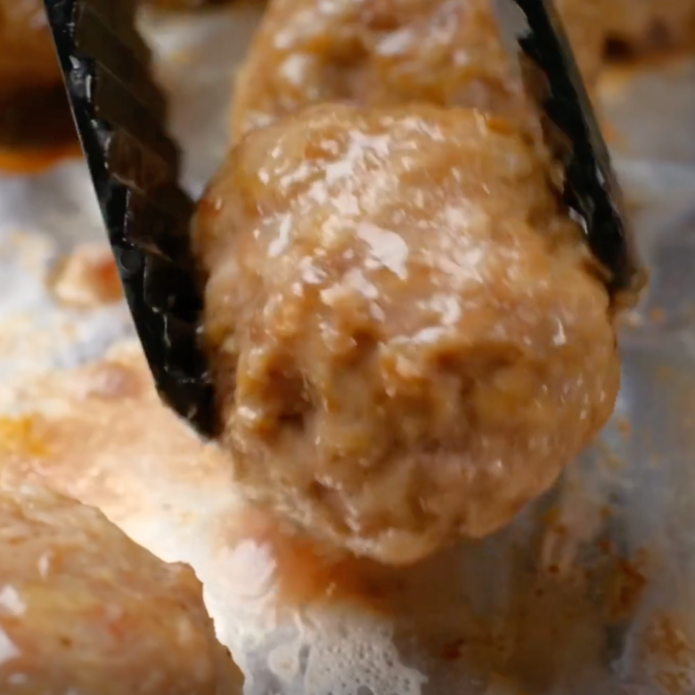 Closeup shot of a Swedish meatball being flipped halfway during baking.