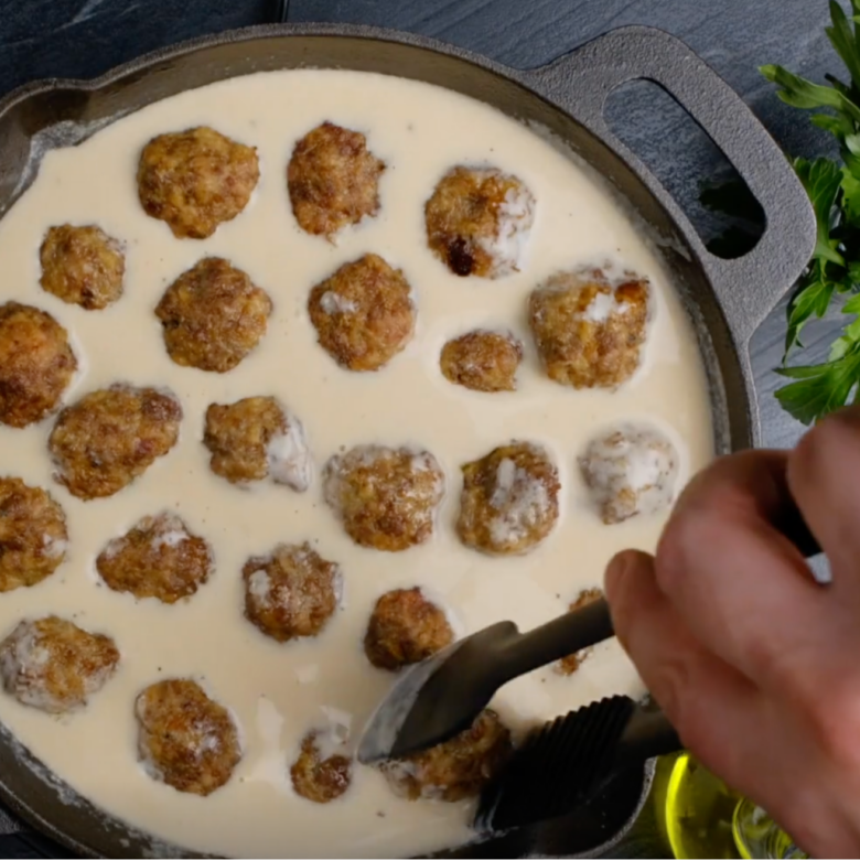 Overhead shot of Swedish meatballs added into gravy mixture and being cooked on the stovetop.