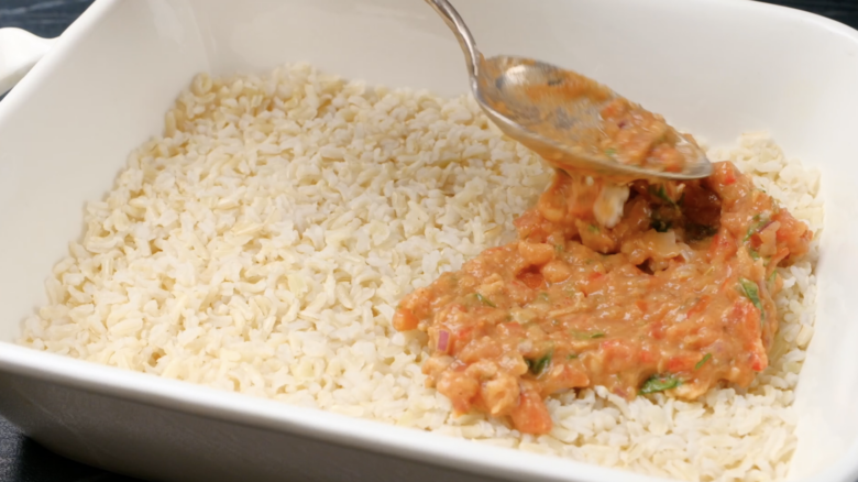 Refried bean and salsa mixture being layers on top of rice in a baking dish.