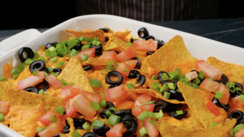 Freshly baked taco casserole being garnished with green onions and tomatoes.