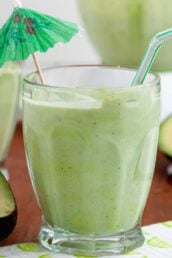 Avocado coconut smoothie with an umbrella and sliced avocado in the background.