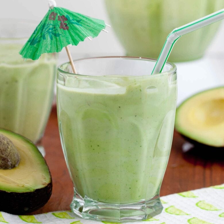 Avocado coconut smoothie with an umbrella and sliced avocado in the background. 