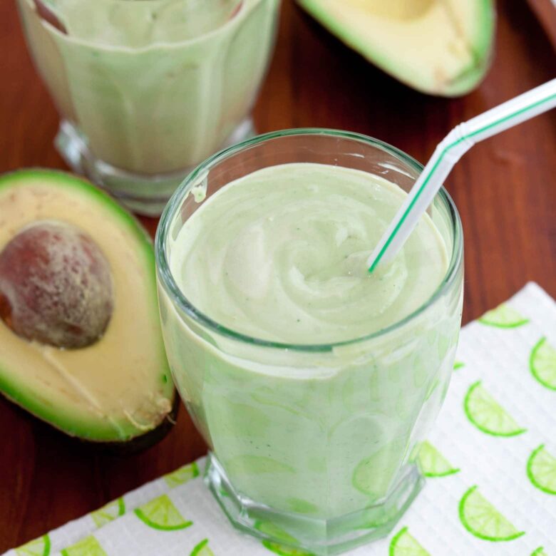 Two glasses of avocado coconut smoothies with a straw.