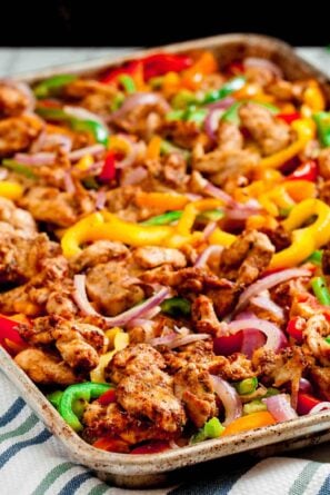 Chicken fajitas on a baking sheet with peppers and onions.