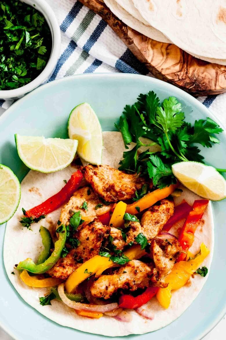 Sheet pan chicken fajitas on tortilla with lime wedges and fresh cilantro on a plate. 