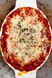 Overhead shot of cheesy baked tortellini in a white oval casserole dish, topped with melted cheese and sprinkled with herbs.