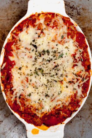 Overhead shot of cheesy baked tortellini in a white oval casserole dish, topped with melted cheese and sprinkled with herbs.