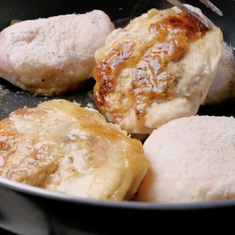 Pieces of chicken being cooked in a pan to make chicken cacciatore.