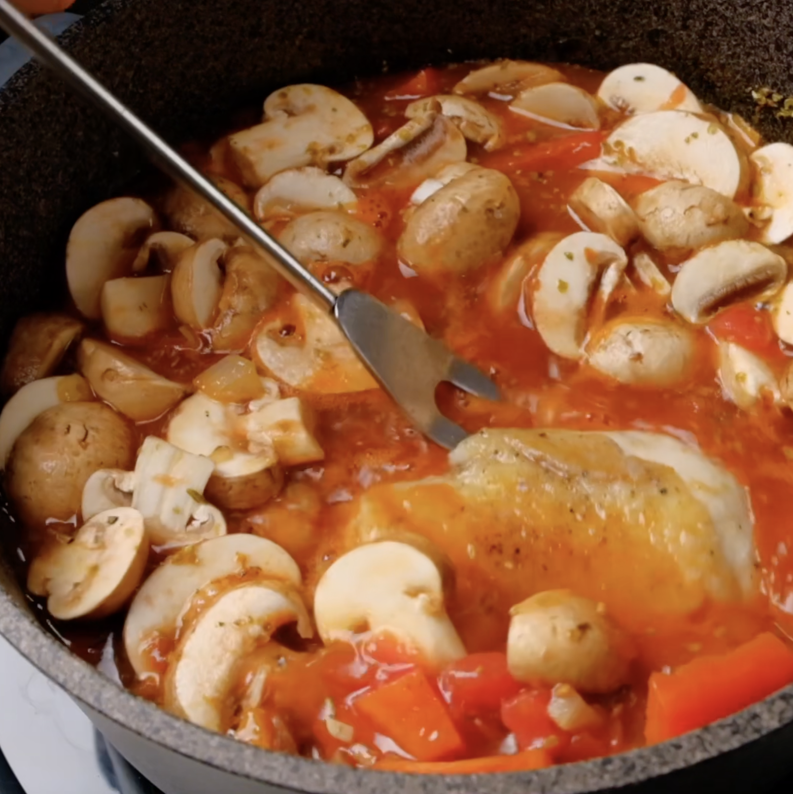 Chicken being added to a pot with tomato-based sauce and mushrooms. 