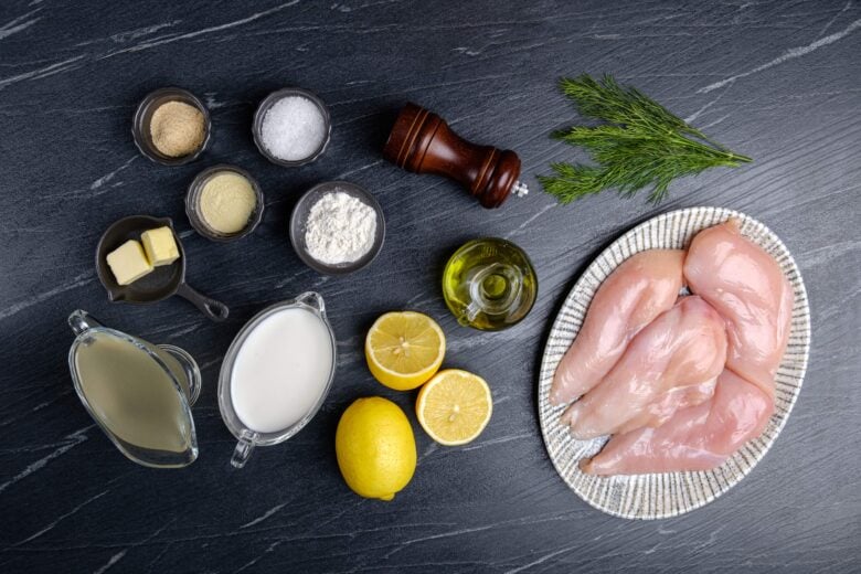 Overhead shot of ingredients to make creamy lemon chicken on a black surface.