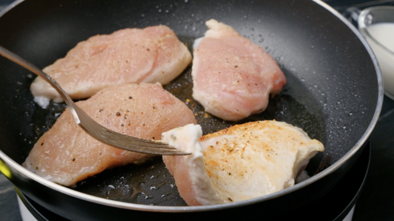 Chicken breasts in a frying pan with a fork.