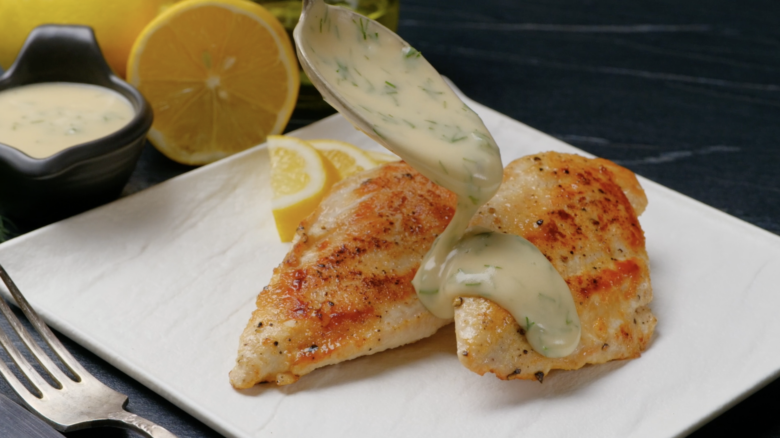 Creamy lemon sauce being poured over skillet chicken.