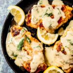 Chicken breasts with lemon sauce in a skillet with sliced lemon and dill.