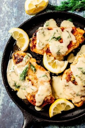 Chicken breasts with lemon sauce in a skillet with sliced lemon and dill.