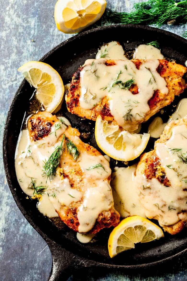 Cooked chicken breasts with lemon sauce in a skillet with sliced lemon and dill. 