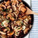 Overhead shot of garlic butter mushrooms in a skillet with a wooden spoon.