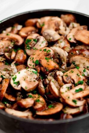 A skillet filled with sauteed mushrooms and herbs.