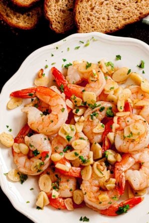Overhead shot of a white plate with garlic shrimp garnished with fresh herbs.