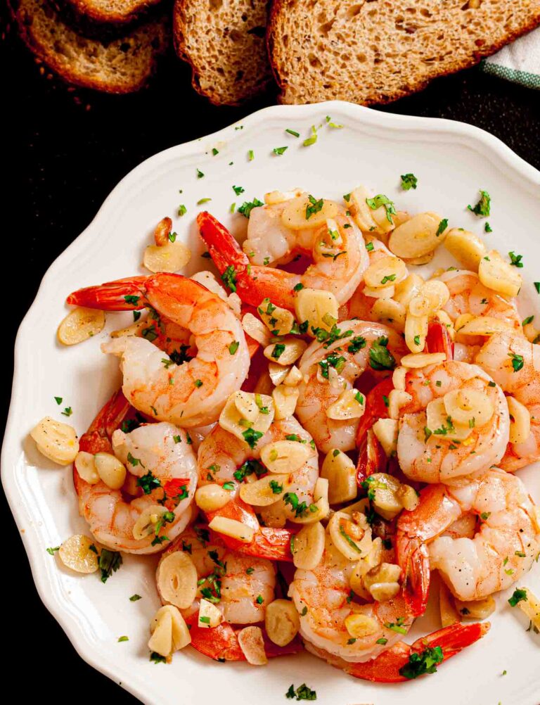 Overhead shot of a white plate with garlic shrimp garnished with fresh herbs.