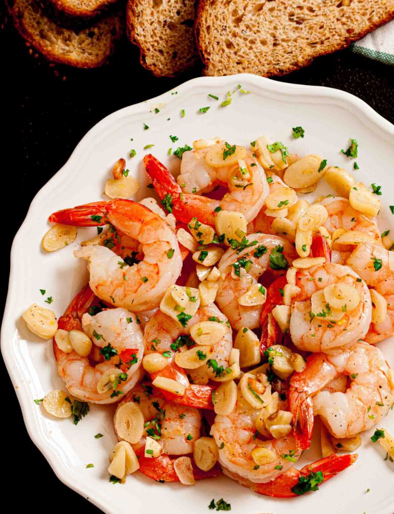 Overhead shot of a white plate with garlic shrimp garnished with fresh herbs. 
