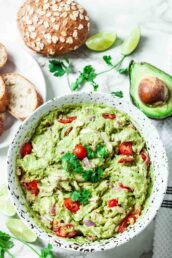 Overhead shot of a a bowl with guacamole chicken salad with tomatoes and bread on the side.