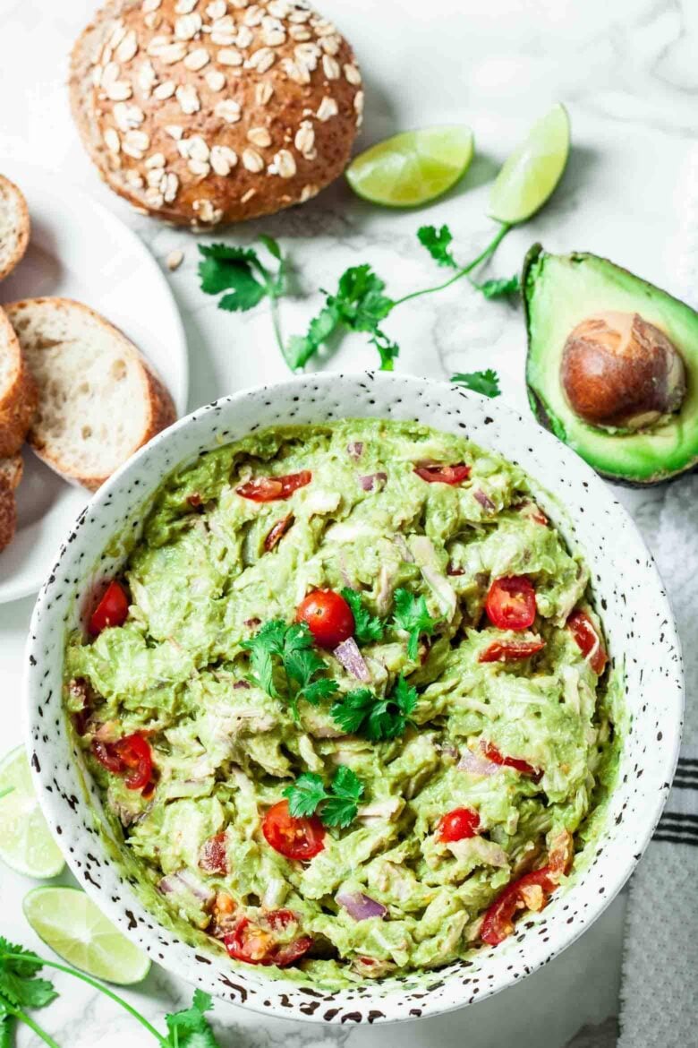 Overhead shot of a a bowl with guacamole chicken salad with tomatoes and bread on the side. 