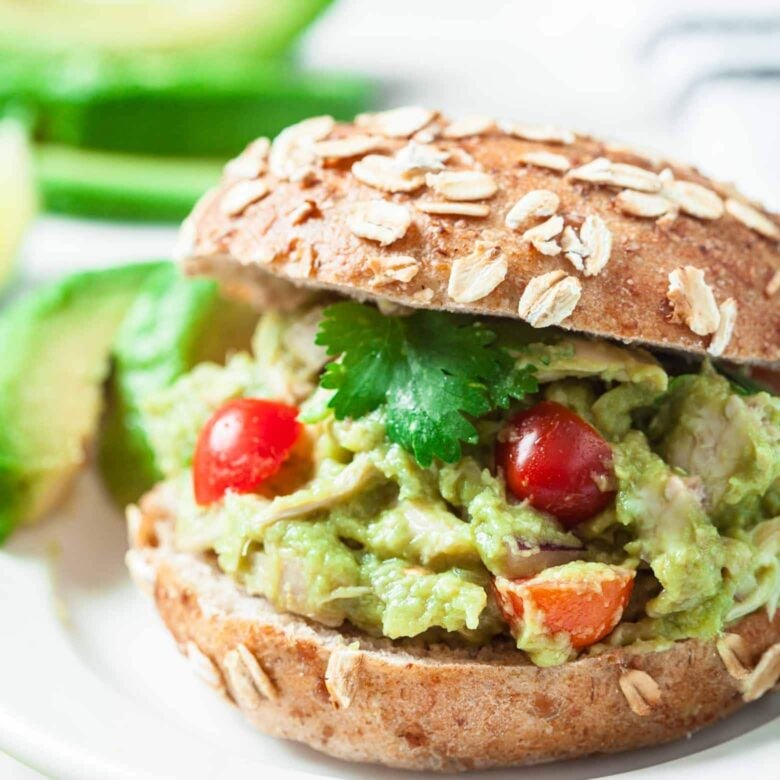 A sandwich with guacamole chicken salad, tomatoes and avocado on a plate.
