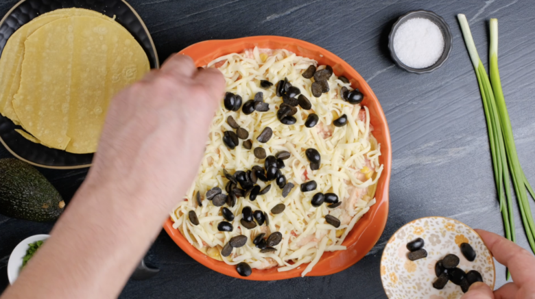 Layered chicken enchiladas being garnished with black olives before baking.