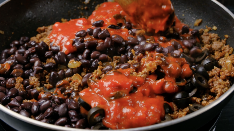A mixture of salsa, black beans, ground beef, and olives being mixed.
