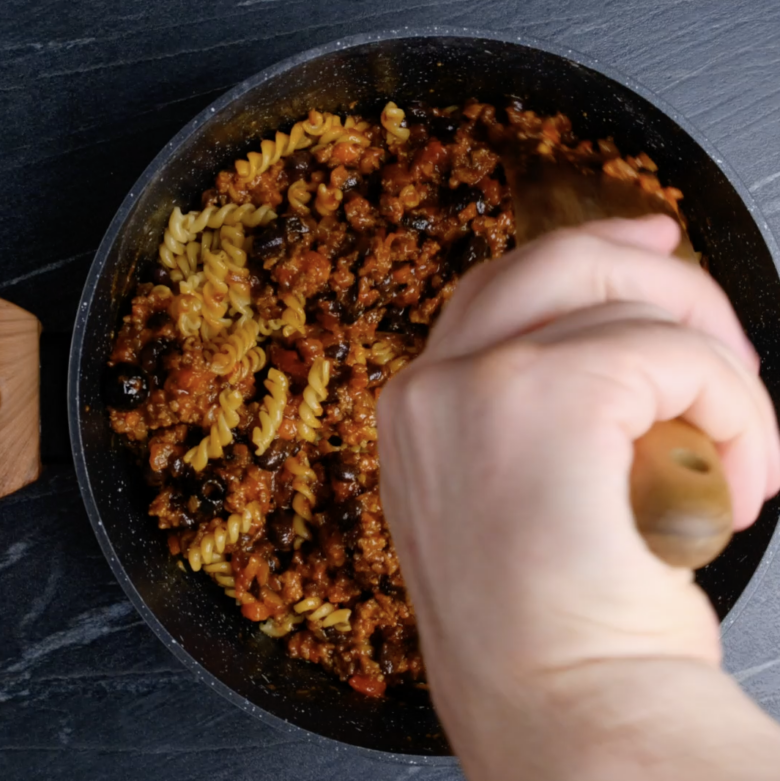 Mexican pasta mixture being mixed with cooked pasta.