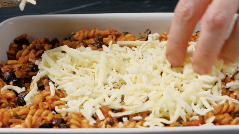Cheese being sprinkled on top of Mexican pasta in a casserole dish.