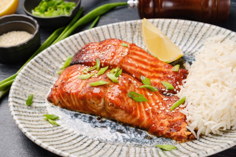 A plate with miso glazed salmon fillets and rice, with a lemon wedge on the side.