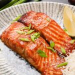 A plate with miso glazed salmon and rice on it with a lemon wedge on the side.