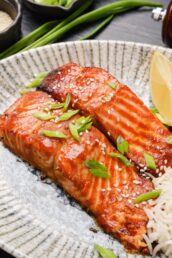 A plate with miso glazed salmon and rice on it with a lemon wedge on the side.