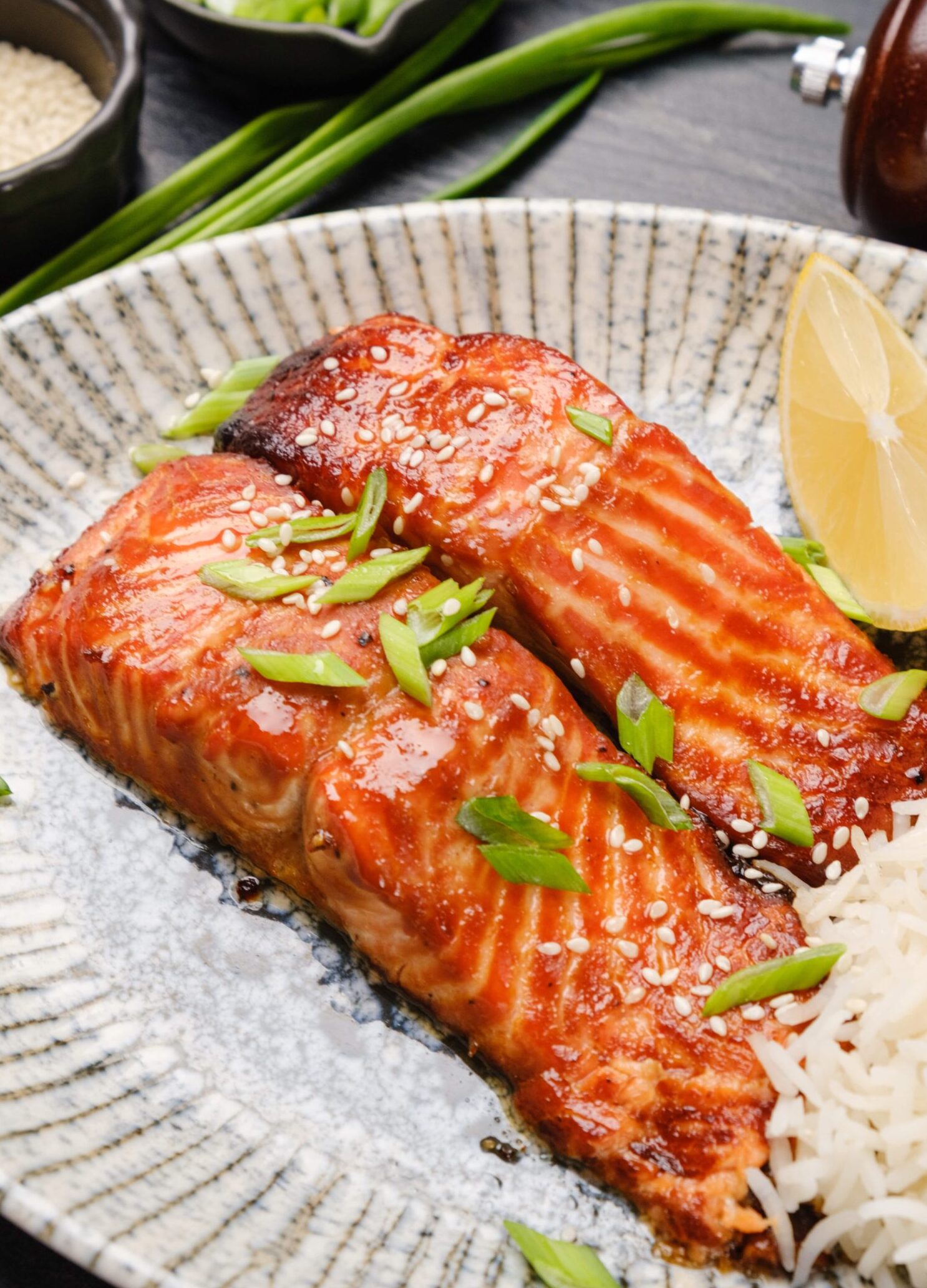 A plate with miso glazed salmon and rice on it with a lemon wedge on the side.