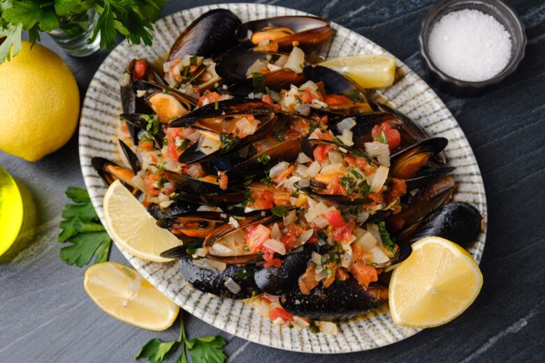 Mussels in white wine sauce on a place with lemon wedges.