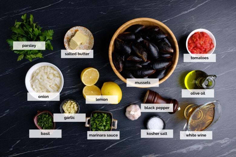 Overhead shot of ingredients to make mussels in white wine sauce on a dark surface.