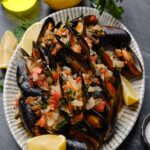 Mussels in white wine sauce on a place with lemon wedges.