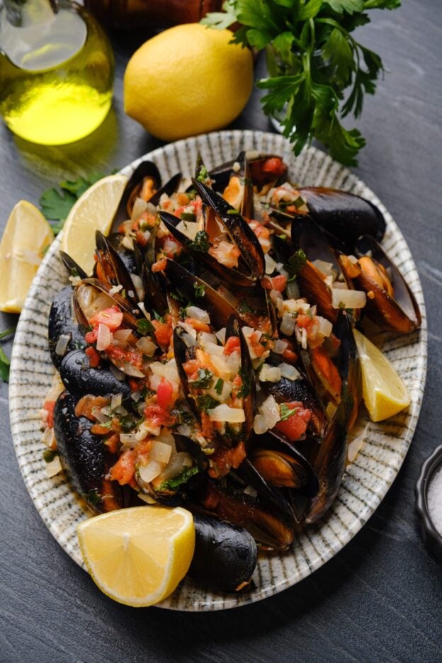 Mussels in white wine sauce on a place with lemon wedges.