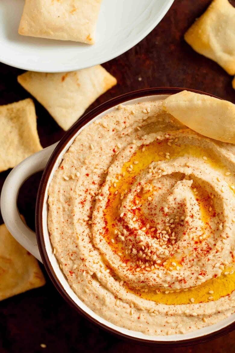 Overhead shot of a bowl of hummus garnished with paprika and sesame seeds with crackers next to it.